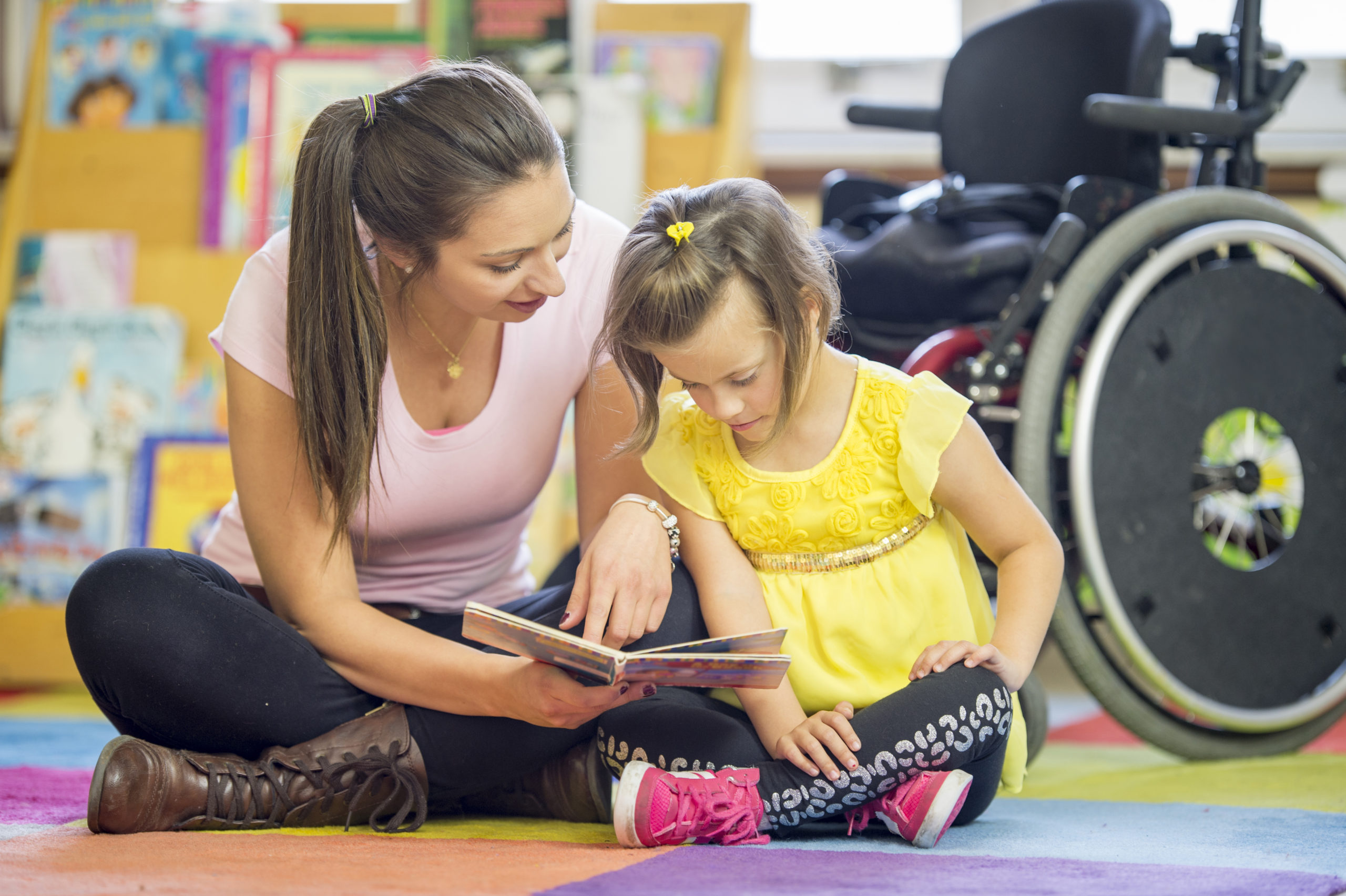 A caregiver and a little girl with are sitting on the floor reading story books together
