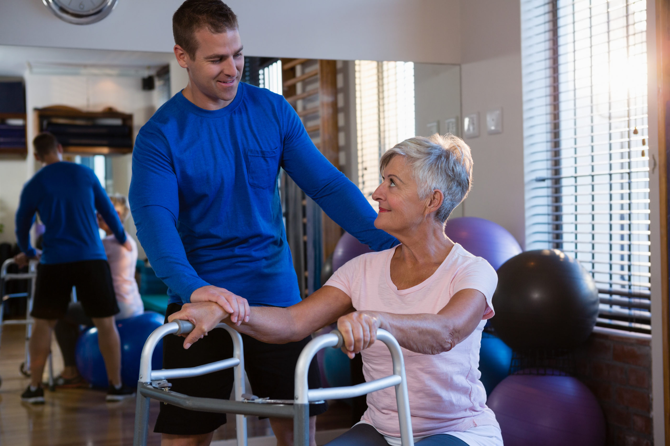 Physiotherapist assisting senior woman patient to walk with walking frame in clinic