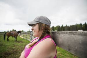 girl outside at farm with horse in background