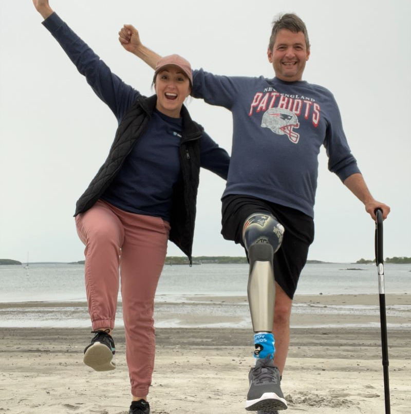 Occupational Therapist Katie McAuliffe with patient Jeff holding a cane on a beach.