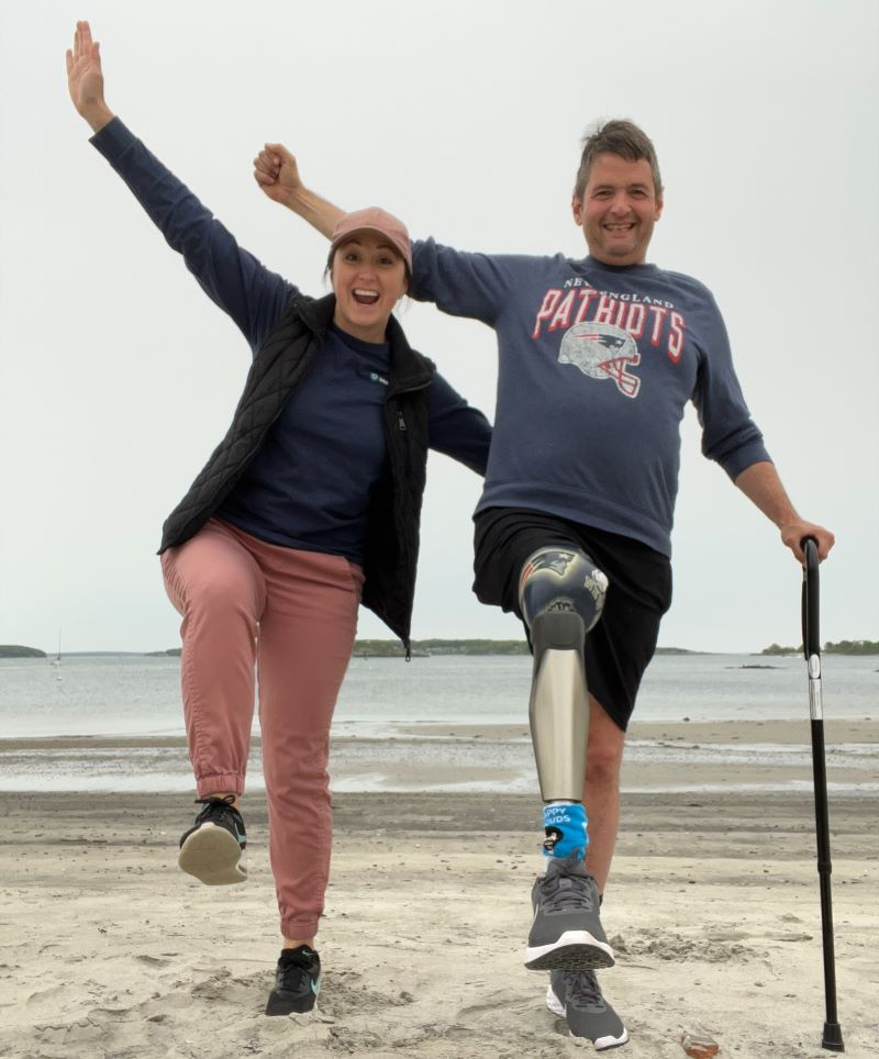 Occupational Therapist Katie McAuliffe with patient Jeff holding a cane on a beach.