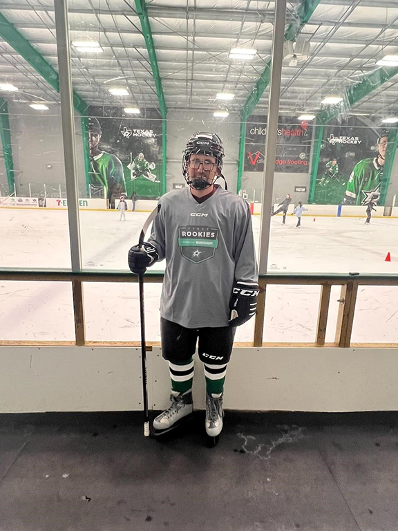Patient William standing at an ice rink in full hockey gear with skates and helmet.