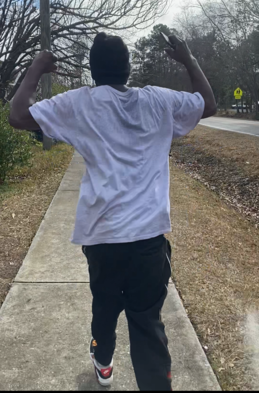 African American man with his back toward camera holding his arms in the air making fists while walking.