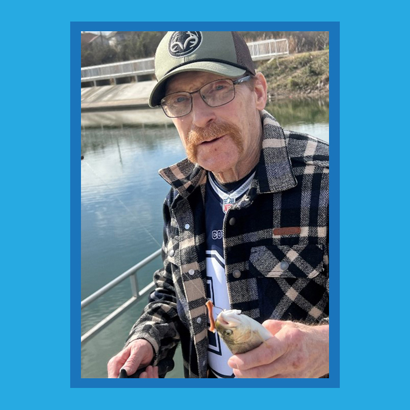 Patient Borden is standing outside on a dock with a lake behind him. He is smiling, wearing a hat, glasses, and flannel sweatshirt. He is holding a fish.