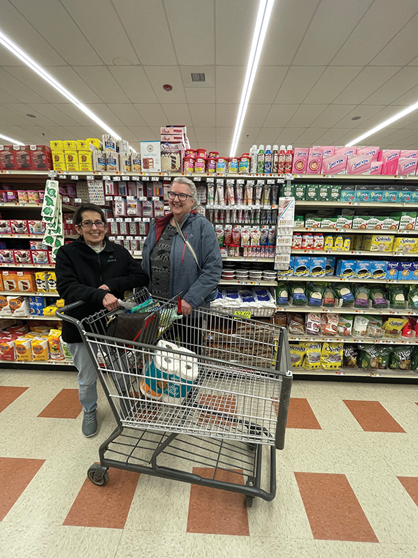 Rene C. standing with her therapist inside a grocery store. Both are smiling holding onto the shopping cart.