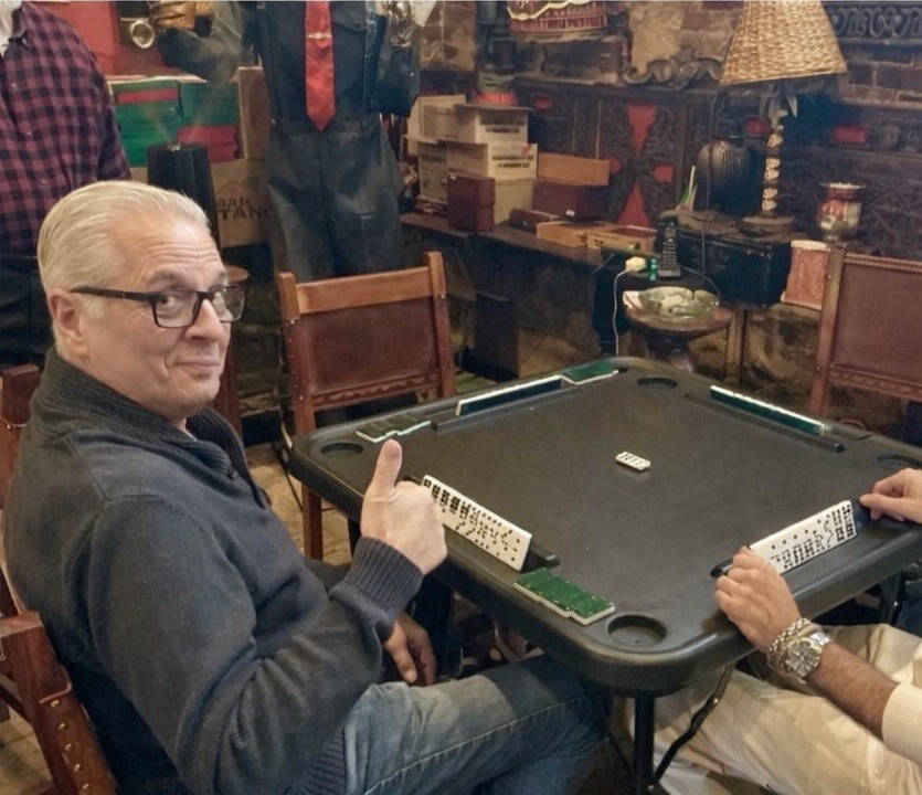 Gary is playing dominoes while giving the thumbs up and smiling at the camera.