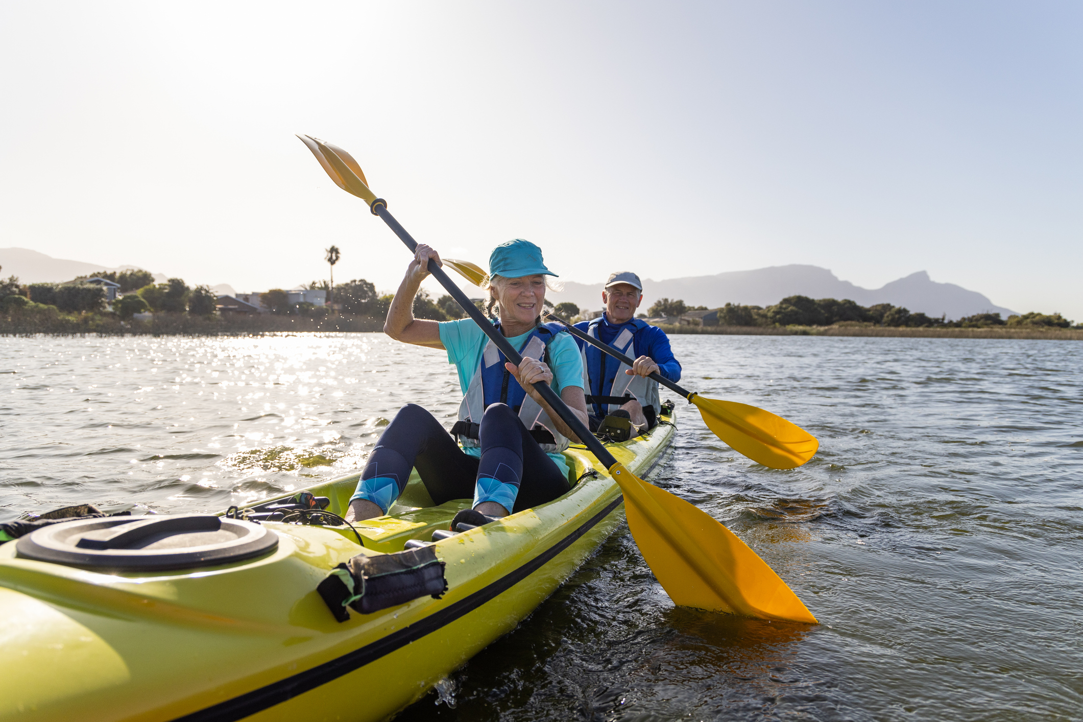 Older couple outside kayaking on a lake together during sunset smiling
